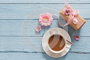 Coffee cup, pink flowers and a gift on pastel blue wood backgrou