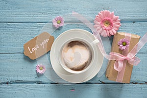 Coffee cup, pink flowers and a gift on pastel blue wood background with copy space, text Love you, top view from above