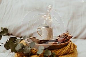 Coffee cup placed on a wooden tray and warm sweater with background bokeh blur of lights. Morning in Bed.