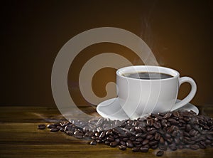 Coffee cup with roasted brown coffee beans and smoke on wooden t