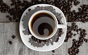 Coffee cup with roasted coffee beans on linen background. Mug of black coffe with scattered coffee beans. Fresh coffee