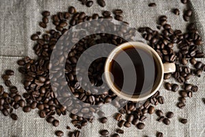 Coffee cup with roasted coffee beans on linen background. Mug of black coffe with scattered coffee beans. Fresh coffee