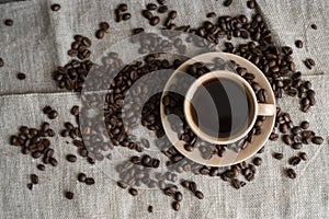 Coffee cup with roasted coffee beans on linen background. Mug of black coffe with scattered coffee beans. Fresh coffee