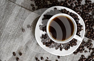 Coffee cup with roasted coffee beans on linen background. Mug of black coffe with scattered coffee beans. Fresh coffee