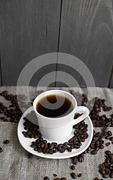 Coffee cup with roasted coffee beans on linen background. Mug of black coffe with scattered coffee beans. Fresh coffee