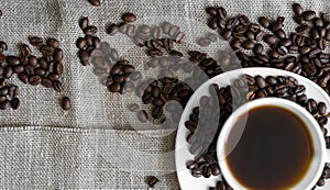 Coffee cup with roasted coffee beans on linen background. Mug of black coffe with scattered coffee beans. Fresh coffee