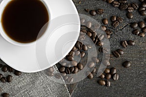 Coffee cup with roasted coffee beans on wooden table background. Mug of black coffe with scattered coffee beans on a