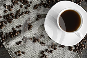 Coffee cup with roasted coffee beans on wooden table background. Mug of black coffe with scattered coffee beans on a