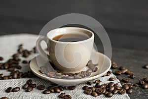 Coffee cup with roasted coffee beans on wooden table background. Mug of black coffe with scattered coffee beans on a