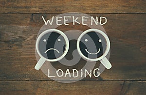 Coffee cup with sad and happy faces next to weekend loading phrase background. vintage filtered. happy weekend concept