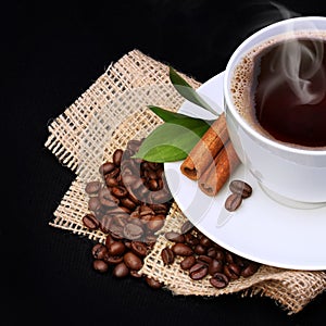 Coffee cup with saucer and coffee beans on burlap over black