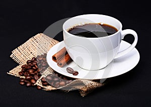 Coffee cup with saucer and coffee beans on burlap over black