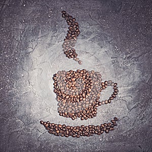 Coffee cup shape from roasted beans with steam on a violet stone background