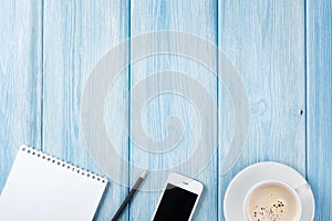 Coffee cup, smartphone and blank notepad on wooden table bac