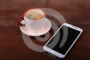 Coffee cup and smartphone on wooden table. View from above