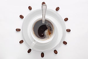 Coffee cup with spoon on saucer and coffee beans against white background forming clock dial viewed from top