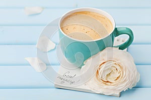 Coffee cup with spring flower and notes good morning on blue rustic background, breakfast