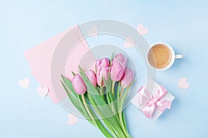 Coffee cup, spring tulip flowers, gift box and pink paper card on blue pastel table top view. Greeting for Womans or Mothers Day.
