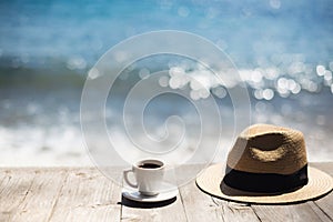 Coffee cup and straw hat on a wood table over a sea background with copy space, travel concept.
