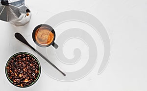 Coffee cup with strong espresso with foam, a coffee pot and coffee beans in a bowl on a white concrete background. Top view with