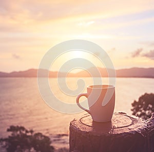 Coffee cup at sunset or sunrise beach in the with lens flare. Wa