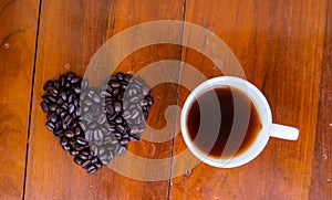 Coffee cup on the table and black rose coffeebean. heart shape bean on wooden table. afternoon refreshing drink for coffee lover.