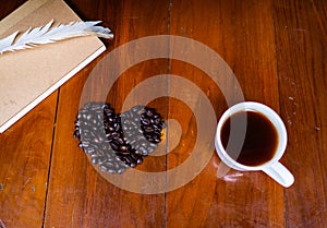 Coffee cup on the table and black rose coffeebean. heart shape bean on wooden table. afternoon refreshing drink for coffee lover.