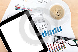 Coffee cup, tablet over papers with numbers and charts
