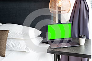 Coffee Cup To Go and a Laptop on the bedside. Technology and home concept. Green template on screen