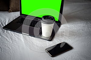 Coffee Cup To Go, Laptop and smartphone on bed. Working from home concept. Green template on screen