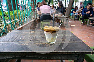 Coffee cup on vintage wooden table. Hot milk coffee outdoor with people drinking coffee on background