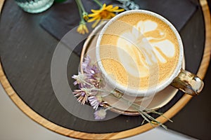 Coffee cup with white gold stands on a saucer with a black tray of flowers. Flat lay.