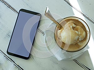 Coffee cup and white smartphone on rustic wooden table. Vintage cafe flat lay composition. Breakfast scene photo