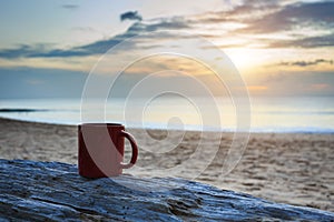 Coffee cup on wood log at sunset or sunrise beach