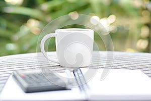 Coffee cup on wood table with calculator, pen and copybook