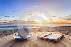 coffee cup on wood table at sunset or sunrise beach