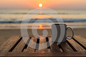 Coffee cup on wood table at sunset or sunrise beach