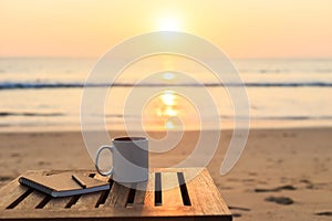 Coffee cup on wood table at sunset or sunrise beach