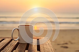Coffee cup on wood table at sunset or sunrise beach