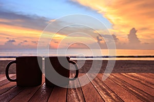 Coffee cup on wood table at sunset or sunrise beach