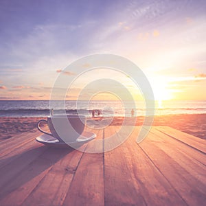 Coffee cup on wood table at sunset or sunrise beach