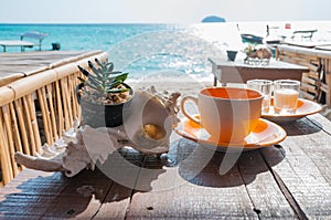 Coffee cup on the wooden table in front of the beach in a beautiful morning sunlight