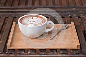 Coffee in a cup on a wooden tray with spoon on a try and place the tray on a metal table