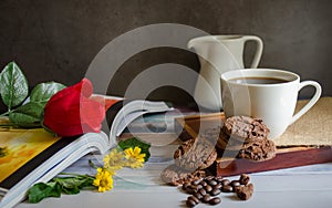 Coffee cups and chocolate chip baked cookies with red roses on books.