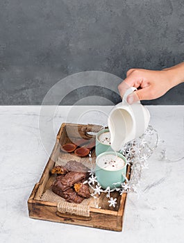 Coffee cups and chocolate coated gingerbread in a wooden basket, pouring milk into a cup, empty copy