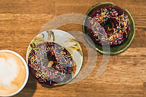 Coffee with a drawn heart and milk on a wooden table in a coffee shop. two chocolate donuts with scattering on the table next to