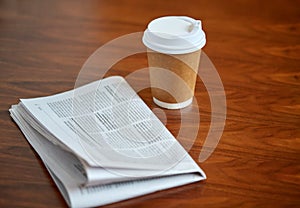 Coffee drink in paper cup and newspaper on table