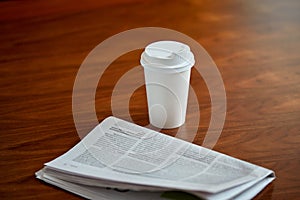 Coffee drink in paper cup and newspaper on table