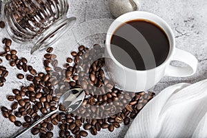 Coffee drink in a white cup and grains on the table top view. Roasted coffee beans