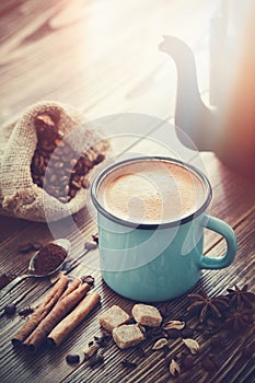 Coffee in enameled cup , sugar cubes, sack of coffee beans and spices.